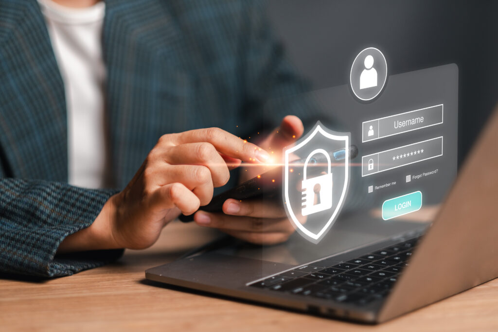 Person typing on a laptop with a virtual cybersecurity shield displaying a login interface.